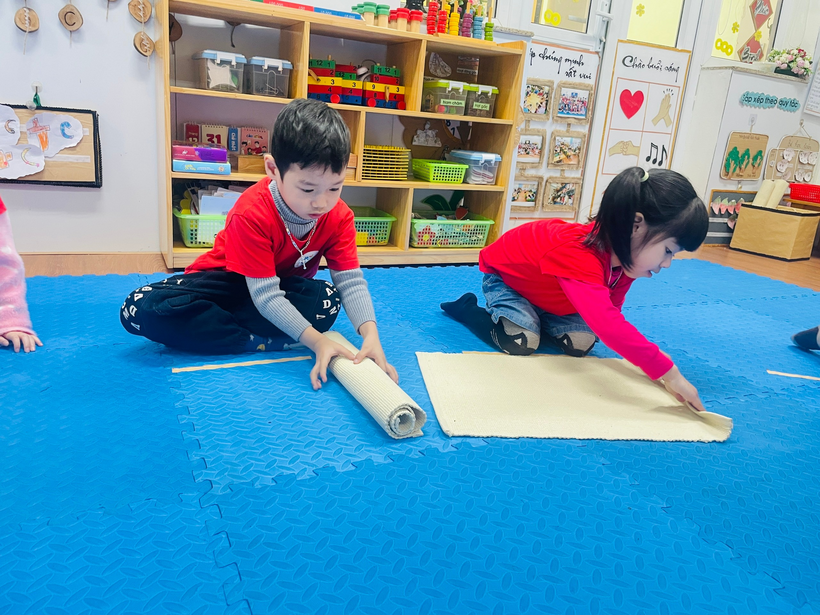 A child and child rolling up a mat

Description automatically generated