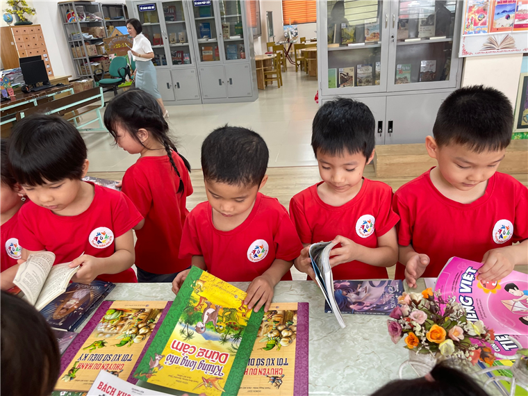 A group of children in red shirts reading booksDescription automatically generated