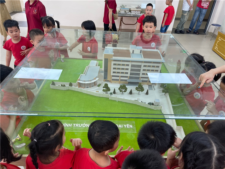A group of children looking at a model of a buildingDescription automatically generated